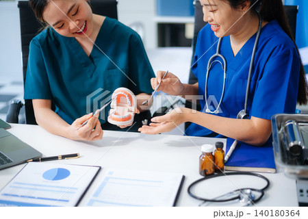 Two dentists in uniform type dental history on laptop with X-ray and tooth model on desk. Modern oral care, teamwork 140180364