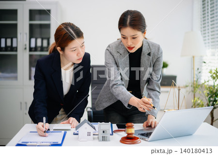 Real estate agent discussing property contract with client, showing house model, agreement, and legal consultation for home buying and investment. Real estate agent discussing property contract with client, showing house model, agreement, and legal consultation for home buying and investment. 140180413