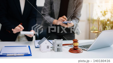 Real estate agent discussing property contract with client, showing house model, agreement, and legal consultation for home buying and investment. 140180416