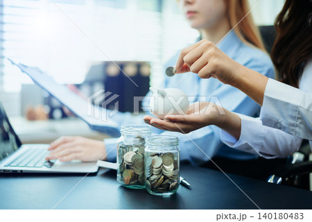 Women saving and counting money with coins, jars, piggy bank, and calculator in office. Finance, budgeting, planning, and smart money Women saving and counting money with coins, jars, piggy bank, and calculator in office. Finance, budgeting, planning, and smart money 140180483