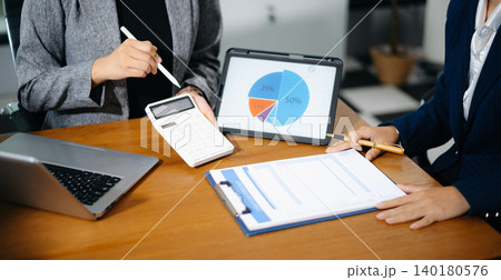 Two businesswomen review cash flow forecast and business growth charts on tablet and clipboard in office. Finance, data analytics, and planning concept for professionals. 140180576