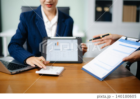 Two professional women in suits reviewing financial charts and analytics on paper and tablet in office. Business analysis, planning, and corporate strategy concept. 140180605