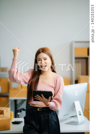 Asian woman prepares parcels and checks online orders on tablet and laptop for delivery online shopping 140181053