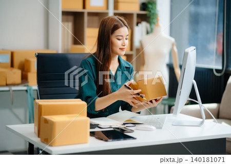 Asian woman prepares parcels and checks online orders on tablet and laptop for delivery online shopping Asian woman prepares parcels and checks online orders on tablet and laptop for delivery online shopping 140181071