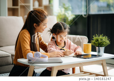 A caring mother and young daughter share a bonding moment doing homework at home. 140181247