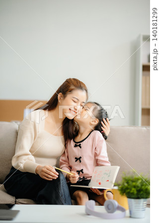A caring mother and young daughter share a bonding moment doing homework at home. A caring mother and young daughter share a bonding moment doing homework at home. 140181299