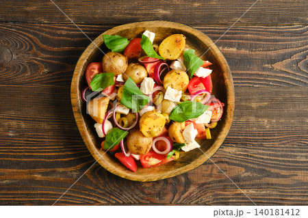 Warm potato and feta salad served in a wooden bowl with fresh vegetables and herbs 140181412