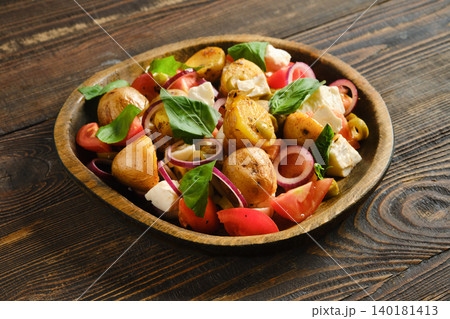 Warm potato and feta salad with tomatoes and herbs served on a wooden plate Warm potato and feta salad with tomatoes and herbs served on a wooden plate 140181413