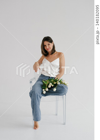 Woman Sitting on Transparent Chair with White Tulips Bouquet 140182095