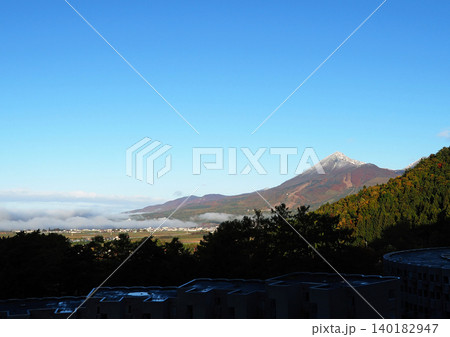 晩秋、朝霧が磐梯山の裾野に漂う。山肌は紅葉し、山頂は薄っすら冠雪して快晴の秋空に印象的で綺麗だ。 140182947