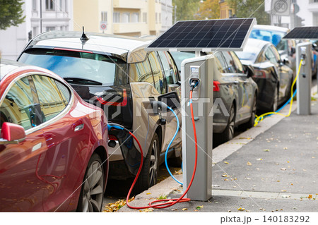 Electric cars are charging from electric vehicle charging stations with built-in solar panels on a city street Electric cars are charging from electric vehicle charging stations with built-in solar panels on a city street 140183292