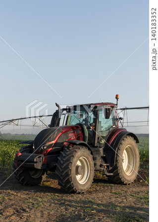 Tractor and agricultural watering pivot irrigation system on a corn field at sunset. Tractor and agricultural watering pivot irrigation system on a corn field at sunset. 140183352