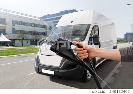 Hand with charging plug on a background of electric van Hand with charging plug on a background of electric van 140183466