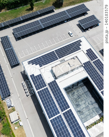 Aerial view of building with solar panels on a roof and parking space with solar canopies. Aerial view of building with solar panels on a roof and parking space with solar canopies. 140183579