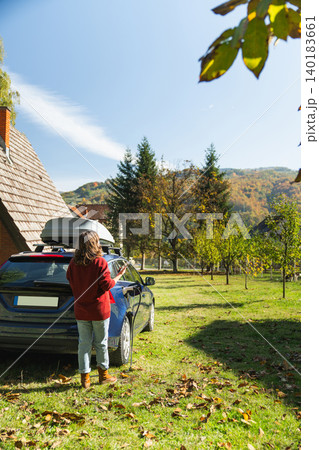 Woman traveler with smartphone next to charging electric car on backyard of country house. Woman traveler with smartphone next to charging electric car on backyard of country house. 140183661