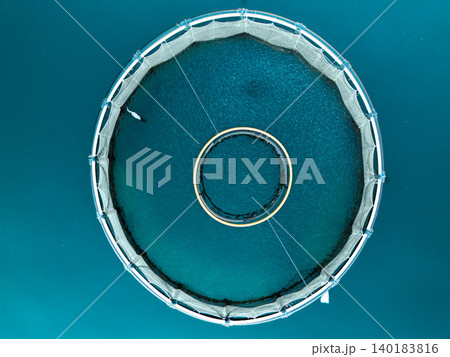 Aerial view of a fish farm with floating cages arranged on the water surface. Modern aquaculture and sustainable seafood production. Aerial view of a fish farm with floating cages arranged on the water surface. Modern aquaculture and sustainable seafood production. 140183816