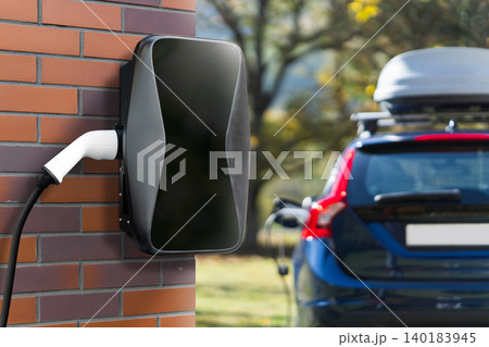 Charging electric car next to countryside house. 140183945