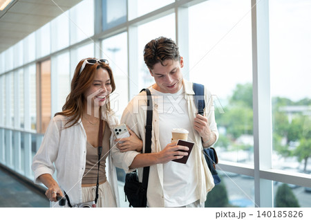 Smiling asian woman girlfriend linking arms talking to white man boyfriend while walking in airport. Smiling asian woman girlfriend linking arms talking to white man boyfriend while walking in airport. 140185826