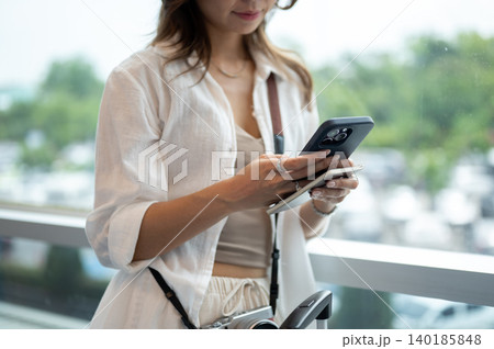 Close up of asian woman holding phone and passport standing beside glass wall in airport's building. Close up of asian woman holding phone and passport standing beside glass wall in airport's building. 140185848