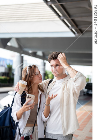 Confused asian woman girlfriend and white man boyfriend holding his head while standing in airport. Confused asian woman girlfriend and white man boyfriend holding his head while standing in airport. 140185991