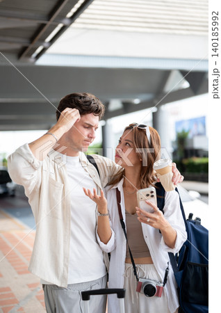 Confused asian woman girlfriend looking at white man boyfriend scratching head standing in airport. Confused asian woman girlfriend looking at white man boyfriend scratching head standing in airport. 140185992