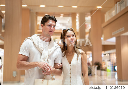 Asian woman girlfriend linking arms looking ahead with white man boyfriend walking in shopping mall. Asian woman girlfriend linking arms looking ahead with white man boyfriend walking in shopping mall. 140186010