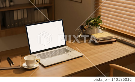 White screen laptop with book and coffee tea cup on wooden table with sunlight through window blinds White screen laptop with book and coffee tea cup on wooden table with sunlight through window blinds 140186036