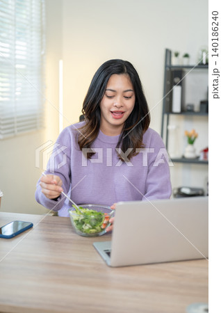 Pretty asian pregnant woman eating salad in front of a laptop on wooden table in living room at home Pretty asian pregnant woman eating salad in front of a laptop on wooden table in living room at home 140186240