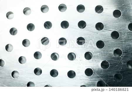 Macro shot of a shiny silver metallic colander surface with circular perforated holes and scratch details, creating a clean industrial pattern Macro shot of a shiny silver metallic colander surface with circular perforated holes and scratch details, creating a clean industrial pattern 140186821