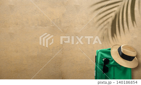 Top view of a green suitcase, straw hat, and sunglasses on sand with palm leaf shadow. Ideal for summer vacation and travel-related concepts with ample copy space 140186854