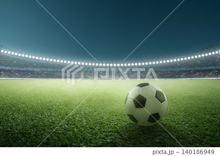 A classic black and white soccer or football ball rests on a lush green grass field under the brilliant floodlights of a large, professional stadium during a night sports event A classic black and white soccer or football ball rests on a lush green grass field under the brilliant floodlights of a large, professional stadium during a night sports event 140186949