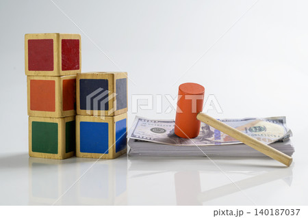 A toy orange wooden gavel on a stack of US hundred-dollar bills next to colorful building blocks, representing child custody costs, education savings, or family court A toy orange wooden gavel on a stack of US hundred-dollar bills next to colorful building blocks, representing child custody costs, education savings, or family court 140187037