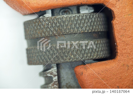 A macro shot showing the textured knurled adjustment metal wheel of an orange plumbing pipe wrench, capturing the detailed metalwork and signs of wear 140187064