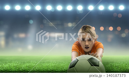 A Indonesian southeast asian female soccer or football goalkeeper in an orange jersey dives to catch the ball on a green field under bright stadium floodlights 140187373