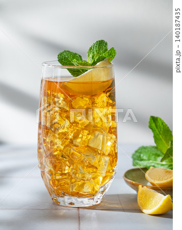 Iced tea with lemon and mint in a glass on a light tile background with shadows 140187435