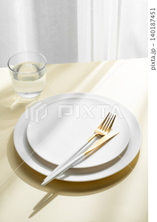An empty white plates with glass of water, fork, knife on a yellow background 140187451