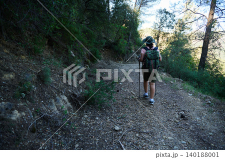 Woman hiking on forest trail with backpack and trekking poles Woman hiking on forest trail with backpack and trekking poles 140188001