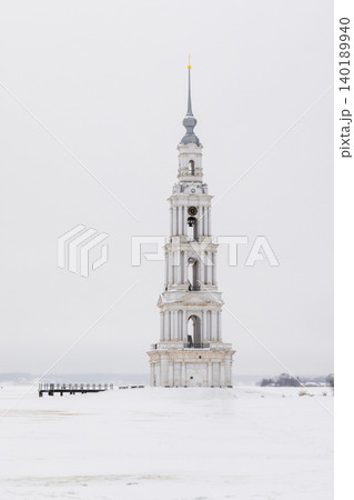 Vertical photo of a tall white bell tower rises alone on a frozen, snow-covered Volga river Vertical photo of a tall white bell tower rises alone on a frozen, snow-covered Volga river 140189940