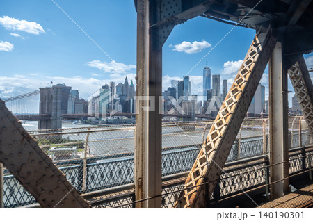New york, usa august 21,2024. Downtown manhattan skyscrapers and landmarks visible through the iconic brooklyn bridge steel trusses over the east river New york, usa august 21,2024. Downtown manhattan skyscrapers and landmarks visible through the iconic brooklyn bridge steel trusses over the east river 140190301