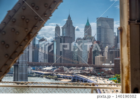 New york, usa august 21,2024. Manhattan skyline framed by brooklyn bridge steel structure, east river and busy highway traffic under a sunny blue sky New york, usa august 21,2024. Manhattan skyline framed by brooklyn bridge steel structure, east river and busy highway traffic under a sunny blue sky 140190302