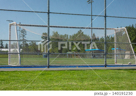 Green soccer Field and football goals Behind Chain Link Fence on a stadium. An empty outdoor football pitch with green artificial turf, white markings, a goalpost, and enclosed by high netting 140191230