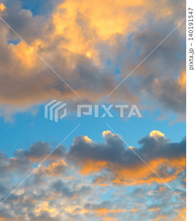Premium vertical view of a beautiful dramatic sky filled with thick sunset clouds illuminated by bright orange golden hour light against a calm blue background. Premium vertical view of a beautiful dramatic sky filled with thick sunset clouds illuminated by bright orange golden hour light against a calm blue background. 140191547