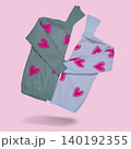 Two cozy knitted turtleneck sweaters with pink heart patterns in grey and light blue colors flying on pastel pink background, copy space. 140192355