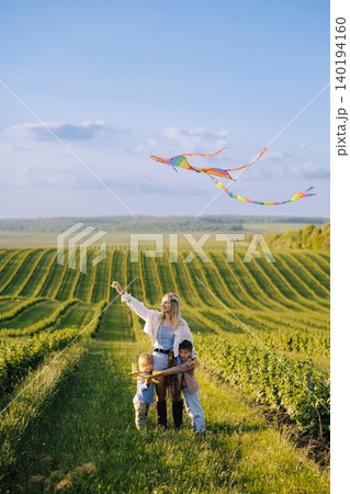 Family flying rainbow kite in a green field 140194160