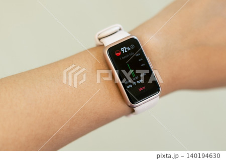 Smartwatch displays heart rate and activity data. Wristband is light pink, sleek and modern. User wears casual clothing, relaxed posture. Screen shows vibrant red and black digital interface Smartwatch displays heart rate and activity data. Wristband is light pink, sleek and modern. User wears casual clothing, relaxed posture. Screen shows vibrant red and black digital interface 140194630