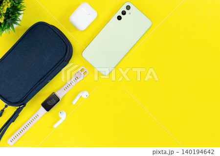 Minimalist tech setup on bright yellow background. Modern smartphone, smartwatch, earbuds, and case neatly arranged. Clean aesthetic suits lifestyle, wellness, or tech-focused content 140194642