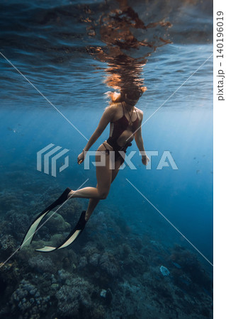 Woman freediver with diving fins underwater in blue water Woman freediver with diving fins underwater in blue water 140196019