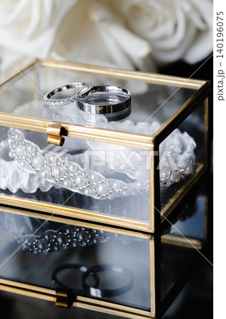 Wedding rings and garter laying in a glass box with white roses in the background 140196075