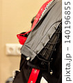 Closeup view of hanging leather garments, black leather piece with red accents. Bright stitching and lacing details, craftsmanship. Decorative for design about making garment 140196855