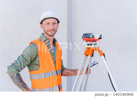 Portrait builder with auto level tool. Engineer man looking at camera working at construction site Portrait builder with auto level tool. Engineer man looking at camera working at construction site 140196906